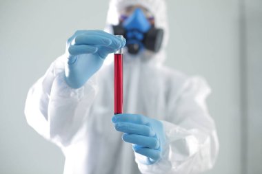 Koruyucu tıbbi giysili bir adam elinde bir test tüpü tutuyor. Coronavirüs 'e karşı açık aşı kavramı