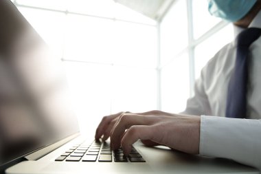 Nefes koruyucu maske takan konsantre genç erkek profesyonel bilgisayar üzerinde çalışıyor.