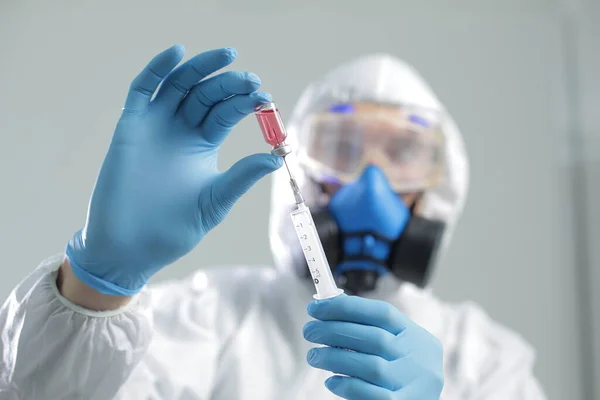 Koruyucu takım elbiseli bir doktor solunum cihazıyla mavi eldivenli bir şırıngadan aşı çeker.