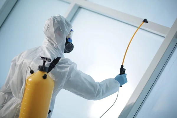 Man in a protective medical suit with a disinfection cylinder in office