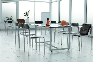 Hoparlör, miğfer, sandalye evrak çantası, cam telefon masası, parlak bir ofis alanı.