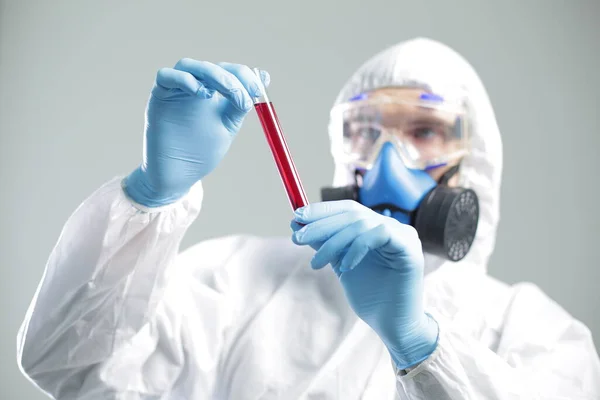 A man in protective medical suit holds a test tube in his hands. The concept of open vaccines against coronavirus