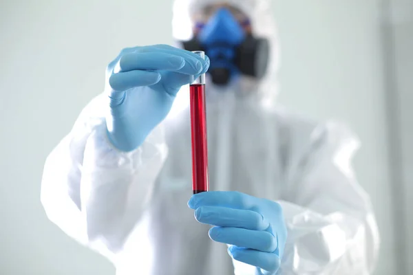 A man in protective medical suit holds a test tube in his hands. The concept of open vaccines against coronavirus