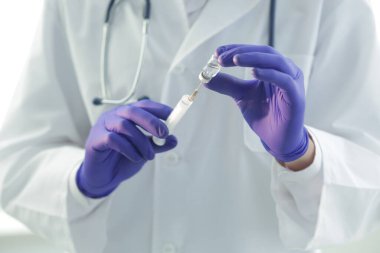 Tıbbi önlüklü ve koruyucu eldivenli bir doktor şırıngayı aşıyla dolduruyor.