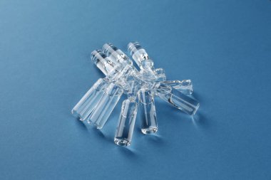 Mavi zemin üzerinde aşı olan cam şişeler.