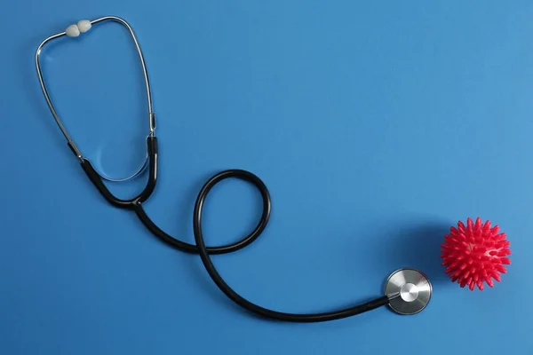 Mavi zemin üzerinde siyah stetoskop ve kırmızı taklit koronavirüs molekülü