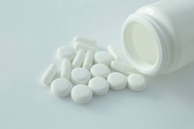 Beyaz arka planda plastik bir şişe ve etrafa saçılmış tıbbi haplar var.