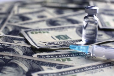 100 dolarlık banknotların arka planında aşı şişesi ve tıbbi şırınga var.
