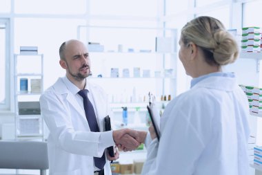 Eczacılar çalışıyor. Erkek ve kadın el sıkışıyor insanlar özel sağlık üniforması giyiyor. Eczaneye yerleştirilen insanlar.