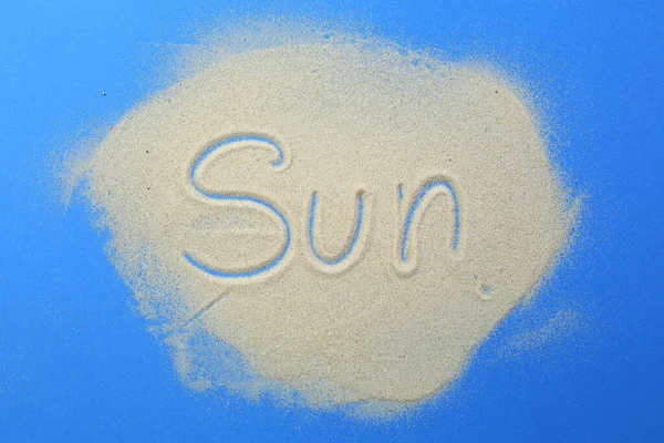 Güneş kelimesi mavi bir arka planda, kuma yazılır.. — Stok fotoğraf