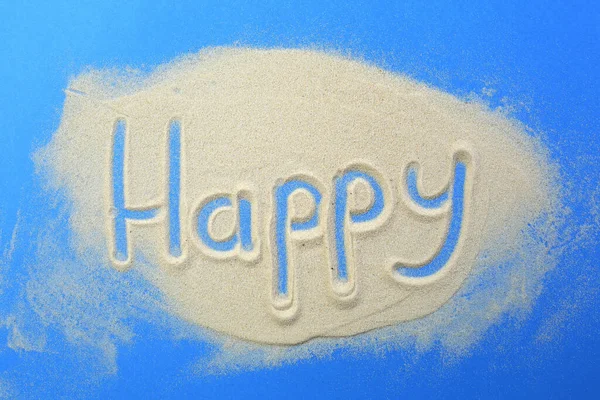 The word happy is written in the sand on a blue background.