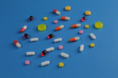 Mavi arka planda çeşitli şekillerde çok renkli tıbbi haplar.