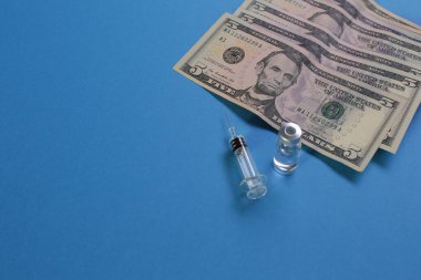 Aşılı şırınga şişesi ve mavi arka planda Amerikan doları.