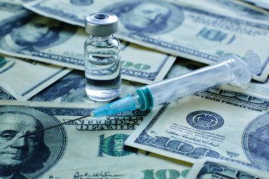 100 dolarlık banknotların arka planında aşı şişesi ve şırınga var.