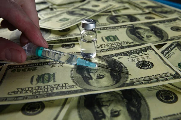 Doctors hand holding a bottle with a vaccine and syringe on a background of one hundred dollar bills