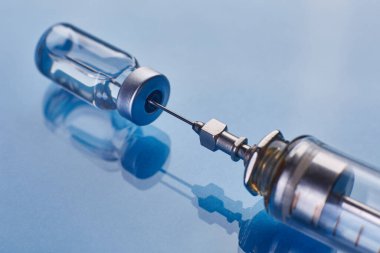 Cam aşı şişesi ve cam şırınga mavi cam arka planda.