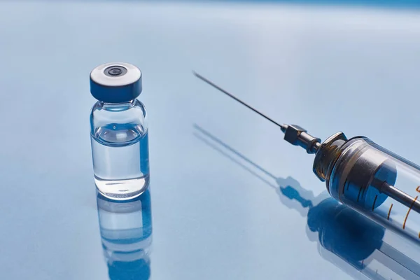 Vial de vacuna de vidrio y jeringa de vidrio sobre fondo de vidrio azul —  Fotos de Stock