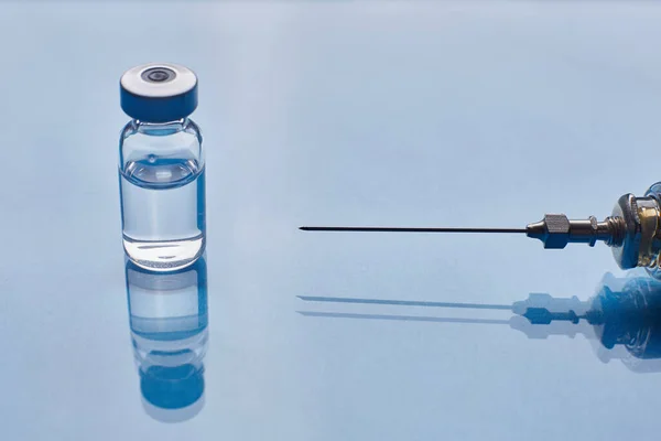 파란 유리 배경 위에 있는 유리 백신 유리병 과 유리 주사기 — 스톡 사진