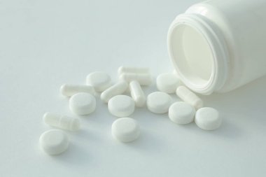 Beyaz arka planda plastik bir şişe ve etrafa saçılmış haplar var.