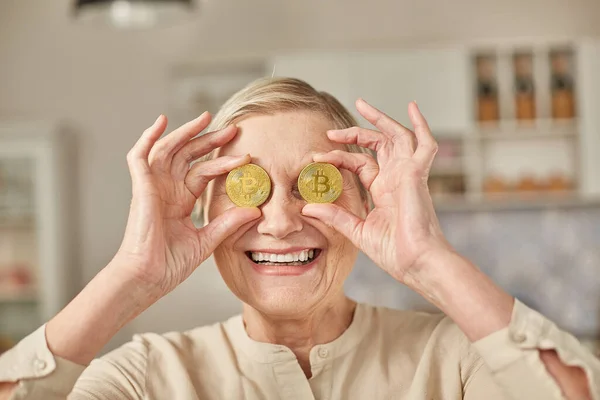 Yaşlı bir kadın, gözlerinin yanında Bitcoin paraları tutuyor. Yaşlılar emeklilik mutlu yaşam konsepti