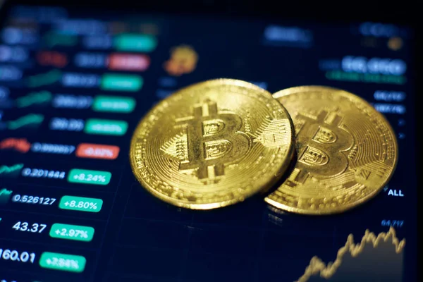 Dos monedas de oro bitcoin se encuentran en la pantalla de la tableta, que muestra indicadores de cambios en las tasas de criptomoneda — Foto de Stock