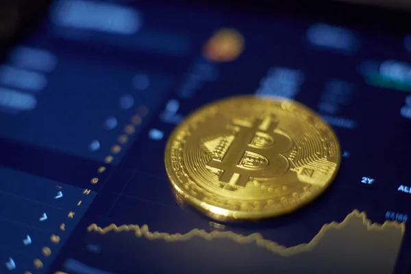 La moneda de oro bitcoin se encuentra en la pantalla de la tableta, que muestra cha — Foto de Stock