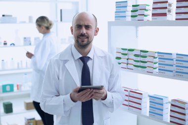 Eczacılar çalışıyor. Erkek ve Kadın. Özel tıp üniforması giyen insanlar. Tableti elinde tutan adam. Eczaneye yerleştirilen insanlar.