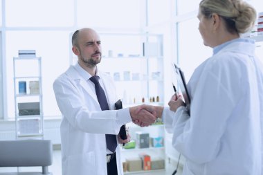 Eczacılar çalışıyor. Erkek ve kadın el sıkışıyor. İnsanlar gülümsüyor. Özel tıp üniforması giyen insanlar. Eczaneye yerleştirilen insanlar.