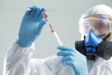 Koruyucu giysili bir doktor solunum cihazıyla mavi eldivenli bir şırıngadan aşı çeker.