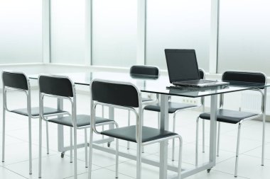 Ofisteki parlak alanda cam masadaki dizüstü bilgisayar.