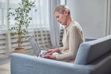 Yaşlı bir kadın bir ürün veya hizmet için dizüstü bilgisayardaki kredi kartıyla ödeme yapar.