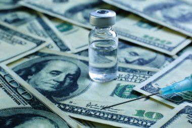 100 dolarlık banknotların arka planında aşı şişesi ve şırınga var.
