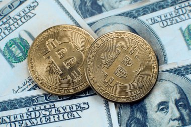 100 dolarlık banknotların üzerinde iki bitcoin kripto para yatıyor.