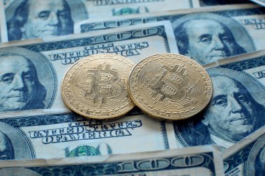 100 dolarlık banknotların üzerinde iki bitcoin kripto para yatıyor.
