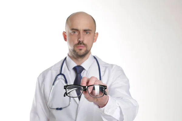 Doktor elinde steteskopla beyaz arka planda gözlük tutuyor.
