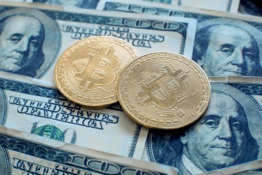 100 dolarlık banknotların üzerinde iki adet bitcoin kripto para yatıyor.