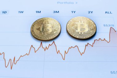 Kripto para biriminin iki altın sikkesi ve kripto para değerlerindeki değişimlerin grafikleri ofisteki ahşap bir masada yatıyor.