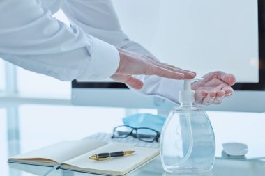 Doktor klinikteki ofisinde çalışıyor ve ellerini dezenfektan kullanarak dezenfekte ediyor.