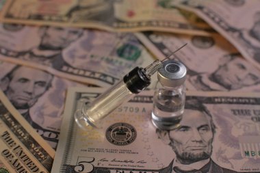 Amerikan dolarlarının arka planında aşı olan tıbbi şırınga şişesi.