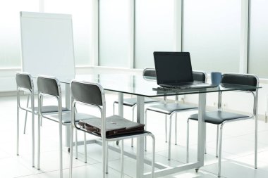 Flipchart dizüstü bilgisayar kahve fincanı telefon evrak çantası cam masa sandalyeleri ofis alanı