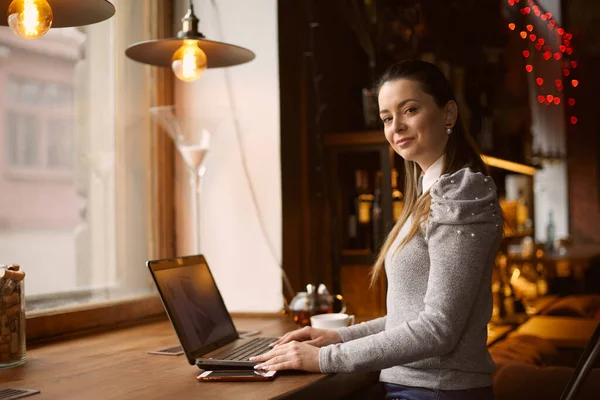 Young girl woman works in a cafe on a laptop performs customer work remotely.