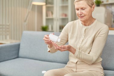 Son sınıf öğrencisi kadın kanepeye oturup günlük vitamin ya da diyet takviyeleri alıyor, olgun yaşlı kadın emekliler ilaç şişesinden, yaşlı sağlık hizmetlerinden bir doz hap alıyor..