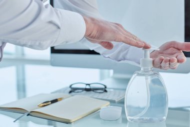 Doktor klinikteki ofisinde çalışıyor ve ellerini dezenfektan kullanarak dezenfekte ediyor.