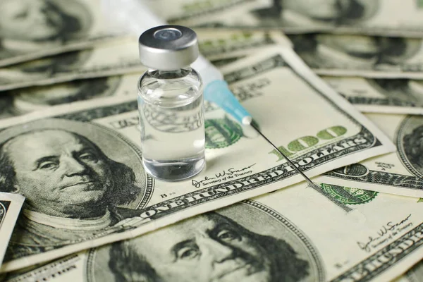 Arkaplanda yüz dolarlık aşı şişesi ve şırınga var.