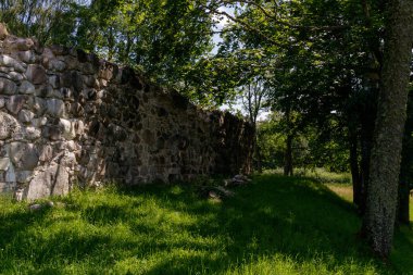 Birçok taştan yapılmış ortaçağ kale tepeciği duvarı. Yaprak döken ağaçlar tarafından gizleniyor. Çok yeşil çimenler ve parlak mavi gökyüzü. Yazın antik bir manzara. Güneşten ve dış dünyadan saklanacak bir yer..