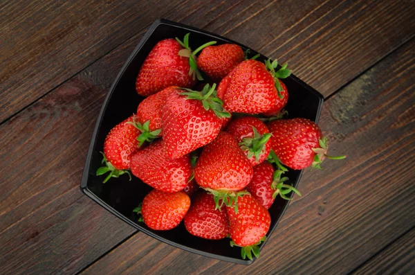 Aardbeien in de zwarte plaat. bovenaanzicht van de houten achtergrond — Stockfoto