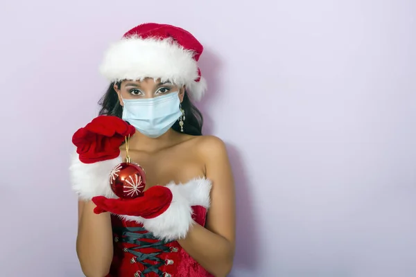 年轻的黑发女人 身穿圣爪服装 戴着外科口罩 手里拿着圣诞球 — 图库照片