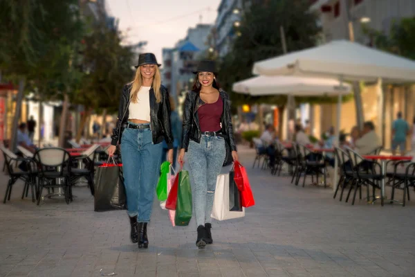 Young girls shopping in the city at dusk, with bags in their hands and happy with their purchase