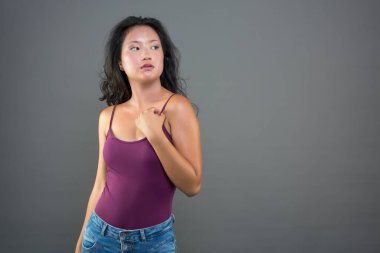 Gri arka plandaki güzel genç Çinli kız, tek başına kenara bakıyor.