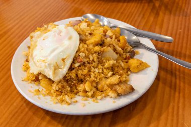 Bir tabak İspanyol migasının yakın çekimi, kızarmış ekmek kırıntıları, domuz eti ve üzeri kızarmış yumurta ile kaplanmış kırsal bir yemek..